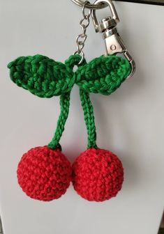 two crocheted cherries are attached to a key chain on a white surface