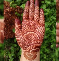 a hand with henna on it is shown in front of some bushes and shrubbery