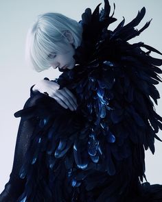 a woman with white hair and black feathers on her body, posing for the camera