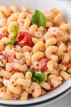 a white bowl filled with macaroni salad and topped with fresh basil on top