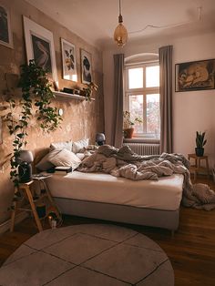 an unmade bed sitting in front of a window next to a potted plant