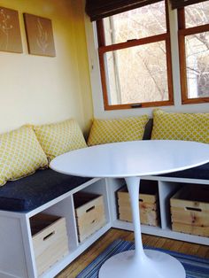 a white table sitting under a window next to a bench with storage boxes on it