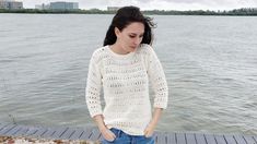 a woman standing on a dock next to the water with her hands in her pockets