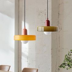 three different colored lights hanging from the ceiling above a dining room table with chairs and a potted plant