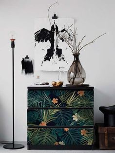 a black and white painting is on the wall next to a dresser with plants in it