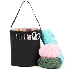 two balls of yarn are next to a black bag with scissors and knitting needles in it