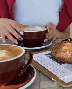 a woman sitting at a table with two cups of coffee and a loaf of bread