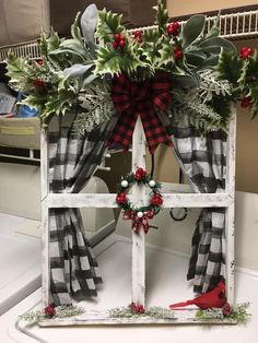 an old window decorated for christmas with red and black plaid ribbon, holly wreaths and cardinal bird