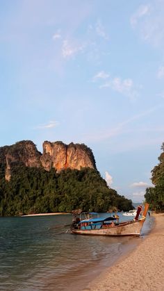 a boat is sitting on the beach next to some trees and water with mountains in the background