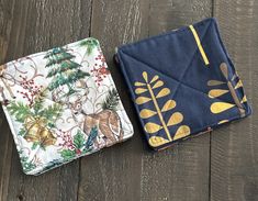 two fabric coasters sitting next to each other on a wooden floor with pine trees and deer