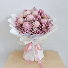 a bouquet of pink roses wrapped in white paper and tied with a ribbon on a wooden table