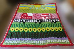 a crocheted table cloth with farm scenes and houses on the top, sitting on a wooden surface