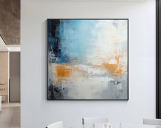 an abstract painting hangs on the wall above a dining room table with white and blue chairs