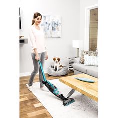 a woman is vacuuming the floor in her living room with a dog sitting on the couch