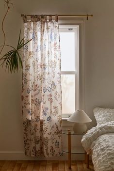 a bedroom with a bed, window and plant in the corner on the table next to it