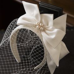 a veiled headpiece with a bow and pearls on the top is sitting on a table