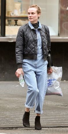 a woman walking down the street with an umbrella in her hand and holding a plastic bag