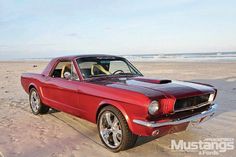 an old red mustang parked on the beach