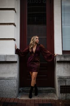 a woman standing in front of a door wearing a purple dress and black booties