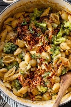 a pot filled with pasta and broccoli on top of a wooden spatula