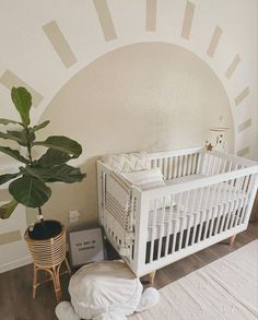 a white crib next to a potted plant in a room with sun painted on the wall