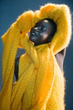 a black mannequin wearing a yellow sweater and holding her head in the air