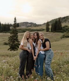 four women standing together in a field with mountains in the background