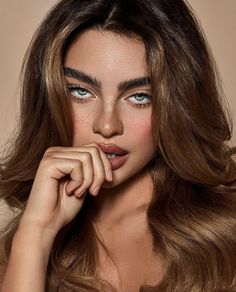 a woman with long brown hair and blue eyes is posing for the camera, her hand on her chin