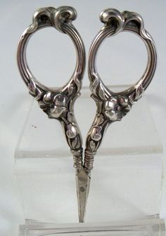 a pair of silver scissors sitting on top of a clear case with a white background