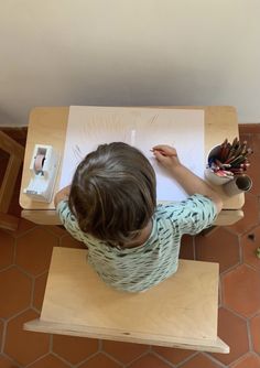 a little boy sitting at a table with some paper and crayons on it