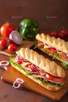 two sub sandwiches cut in half on a cutting board with onions, tomatoes and peppers