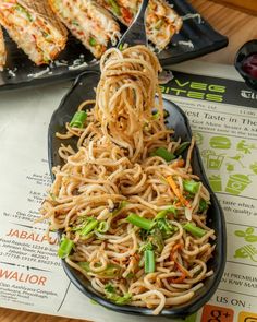 a spoon full of noodles and vegetables on top of a table next to plates of food