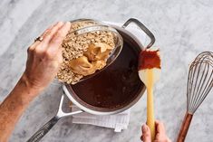 a person holding a whisk in front of a pot filled with oatmeal and peanut butter