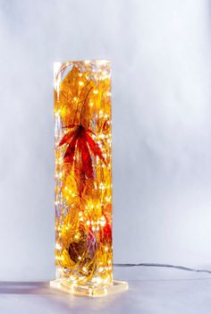 a glass vase with lights in it and leaves on the inside, sitting on a table