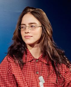 a woman wearing glasses and a red checkered shirt is sitting in front of a blue wall