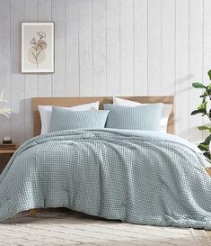 a bed with blue comforter and pillows in a room next to a potted plant