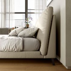 a bed with white sheets and pillows in front of a window next to a wooden floor