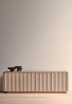 two black bowls sit on top of a wooden cabinet in front of a white wall