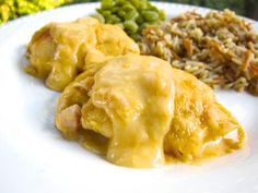 a white plate topped with meat covered in gravy next to rice and peas