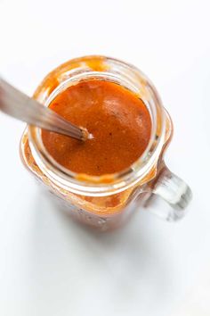 a glass jar filled with red sauce on top of a white table next to a spoon