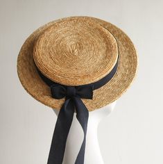 Coco Monroe Hat. Natural Milan Straw Boater Hat by And They Loved Hats. This charming and sporty hat is handcrafted in natural wheat straw. Classic and uncluttered, simply accented with long romantic trailing dark navy ribbon hatband and bow. The boater brim is perfectly flat and has a steel wired brim edge. The interior is fitted with an ribbon lining. This attention to detail and finishing adds lasting quality. The boater attaches with a discreet hair matching millinery elastic.   Casual or fo Adjustable Curved Brim Hat With Ribbon, Adjustable Brimmed Straw Hat For Wedding, Adjustable Ribbon Hat For Kentucky Derby, Adjustable Hat With Ribbon For Kentucky Derby, Classic Adjustable Straw Hat For Weddings, Kentucky Derby High Crown Boater Hat, Adjustable Wide Brim Straw Hat For Wedding, Adjustable Wide Brim Boater Hat For Weddings, Adjustable Brimmed Hat With Ribbon