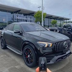 a mercedes benz dealership with cars parked in the lot and someone holding up a cell phone