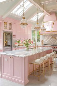 a kitchen with pink cabinets and marble counter tops, gold chandeliers and white stools