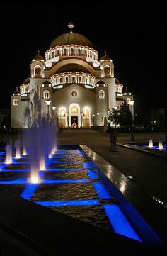 a large building with fountains in front of it at night, lit up by blue lights