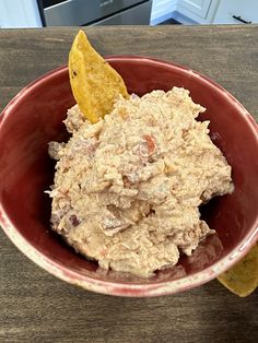 a red bowl filled with food sitting on top of a wooden table next to a potato wedge