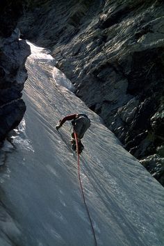 a man climbing up the side of a snow covered mountain next to a red rope