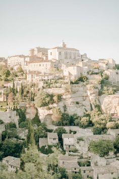 an old town on top of a hill with trees in the foreground and buildings below