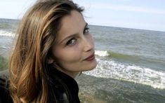 a woman standing in front of the ocean with her hair blowing back and looking off into the distance