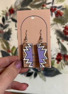 a pair of wooden earrings with purple and white designs on the front, sitting next to a cardboard package