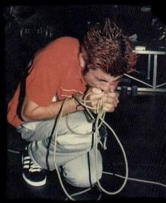 a young man sitting on the ground with his hands in his face and wires coming out of his mouth